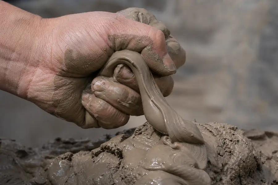 Of a hand squeezing moist clay soil into a shiny ribbon