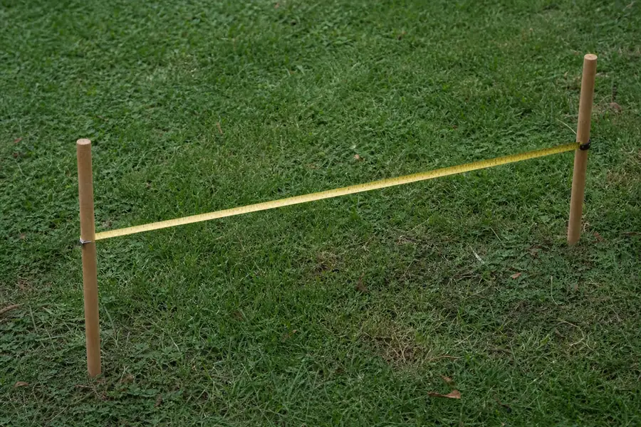 Of a long tape measure stretched across grass between two planting stakes