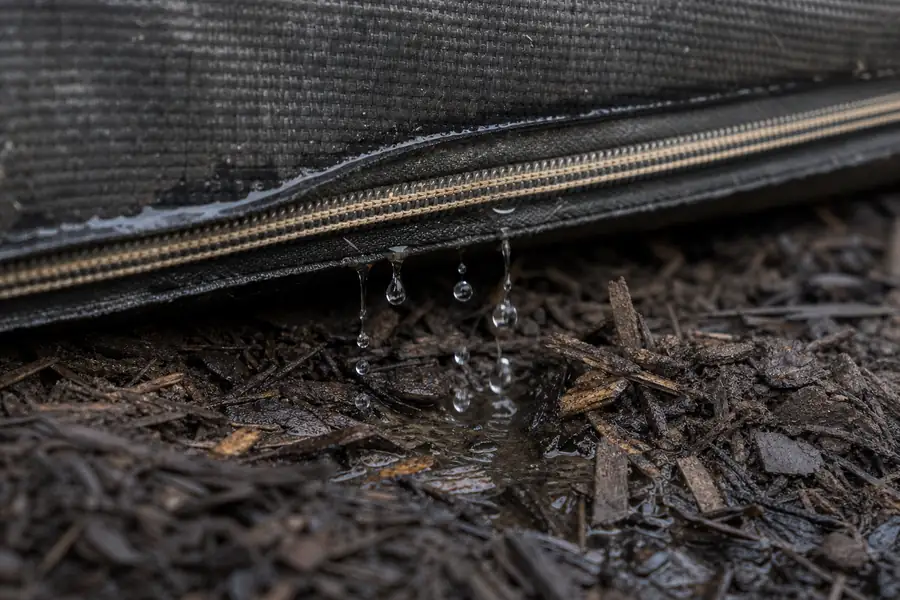 Of a zippered bag seam releasing slow drips onto dark mulch